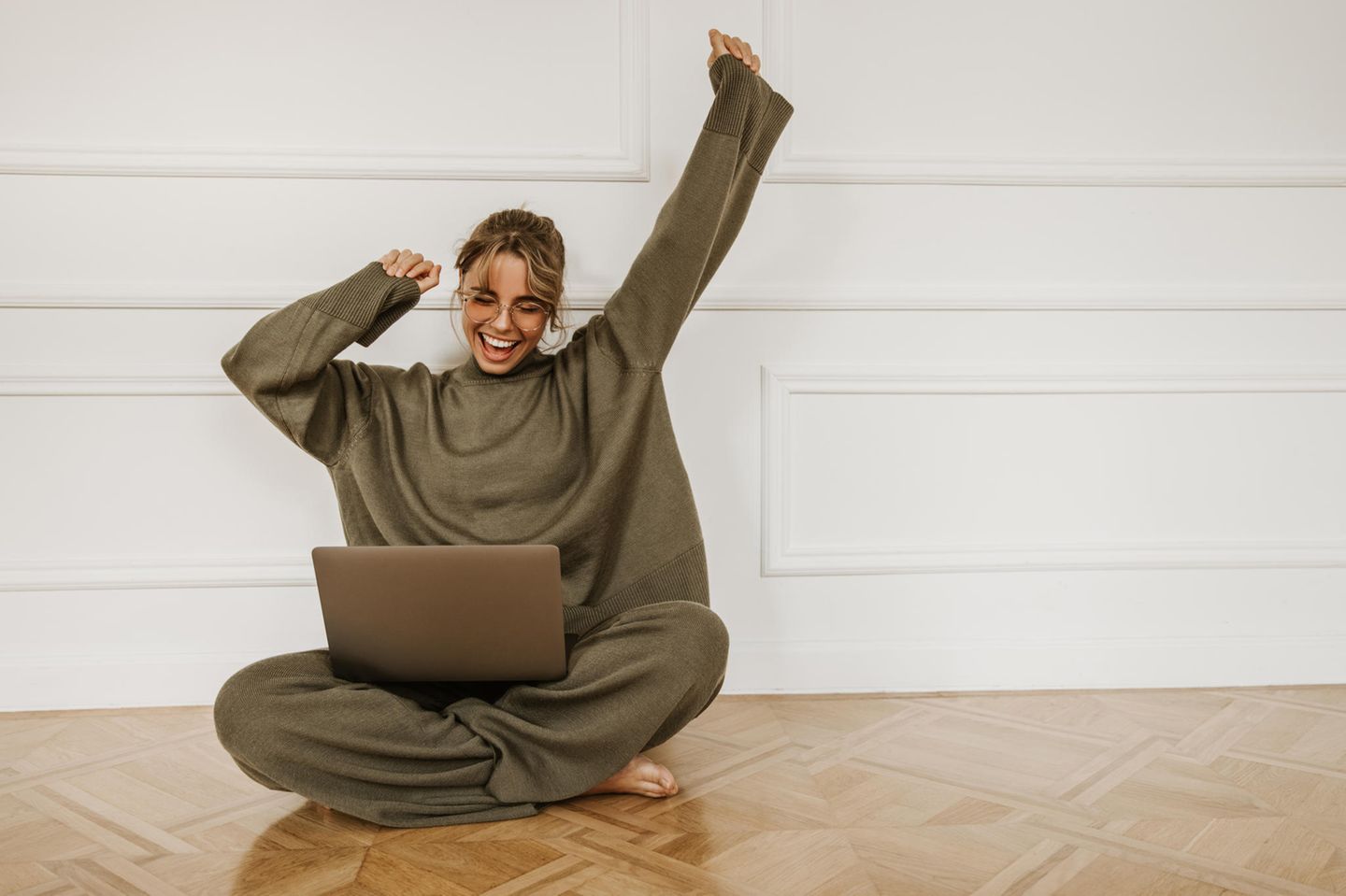 Gesetz der Anziehung: junge Frau sitzt mit Laptop auf Fußboden und freut sich sehr