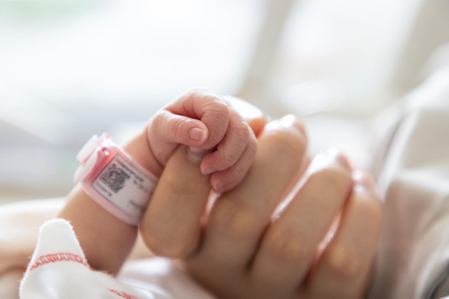 Und dann kamst du: Eine Hand hält die kleine Hand eines neugeborenen Babys