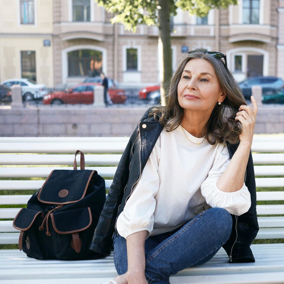 Eine elegant gekleidete Frau sitzt auf einer Parkbank