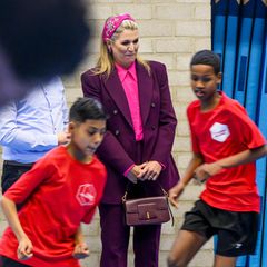 Schon am Vortag setzte die Königin bei ihrem Besuch der VMBO Schule Goudse Waarden in Gouda auf kräftige Farben. Den Zara-Anzug in Aubergine kombiniert sie gekonnt mit einem pinkfarbenen Hemd, und auch die Accessoires passen farblich toll zum royalen Look, besonders das verspielte Haarband von NamJosh.