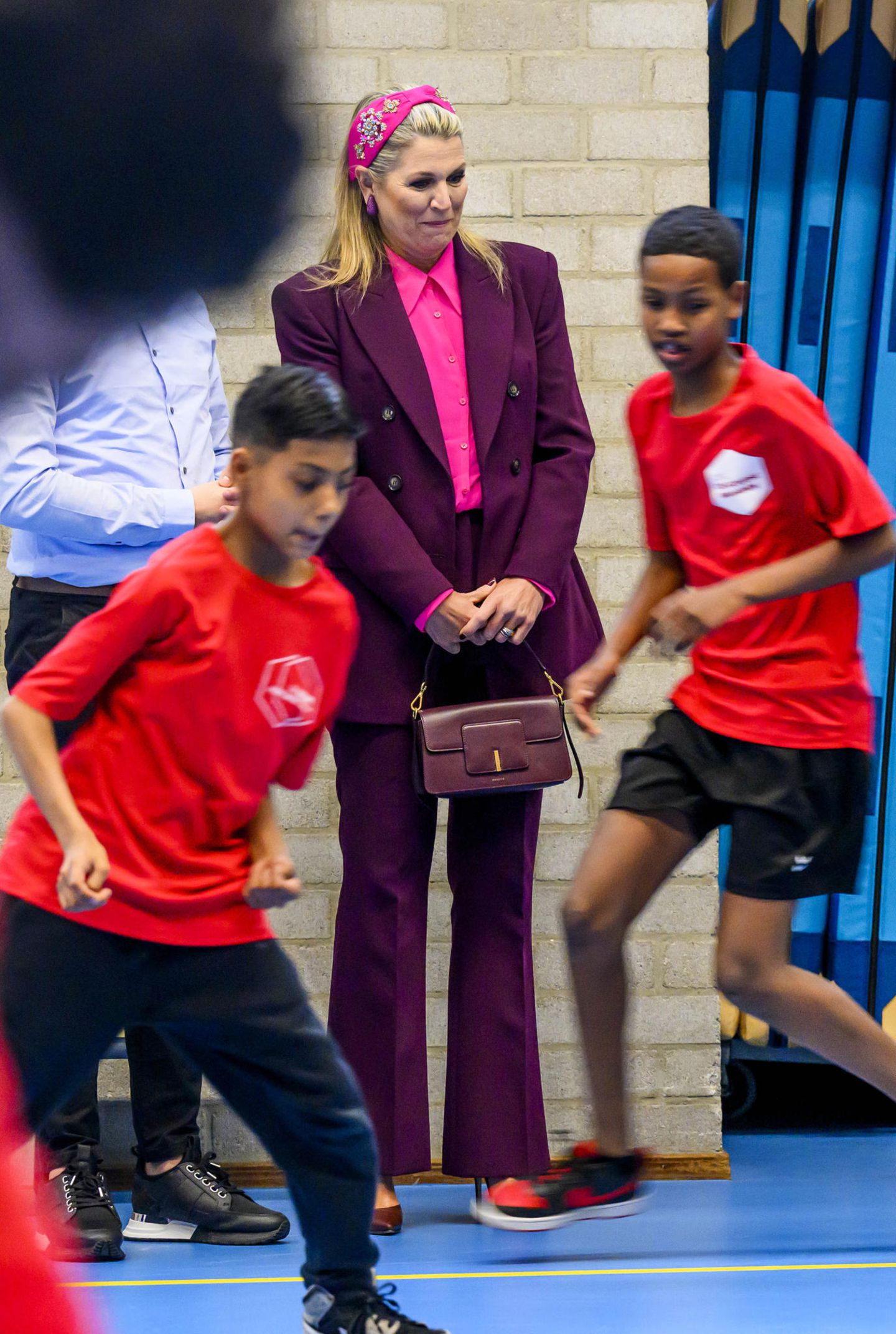Schon am Vortag setzte die Königin bei ihrem Besuch der VMBO Schule Goudse Waarden in Gouda auf kräftige Farben. Den Zara-Anzug in Aubergine kombiniert sie gekonnt mit einem pinkfarbenen Hemd, und auch die Accessoires passen farblich toll zum royalen Look, besonders das verspielte Haarband von NamJosh.