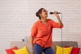 Eine Frau singt mit einem Mikrofon vor einem Sofa