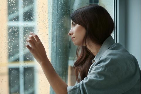 Desorganisierte Bindung: Junge Frau am Fenster, blickt raus, es regnet