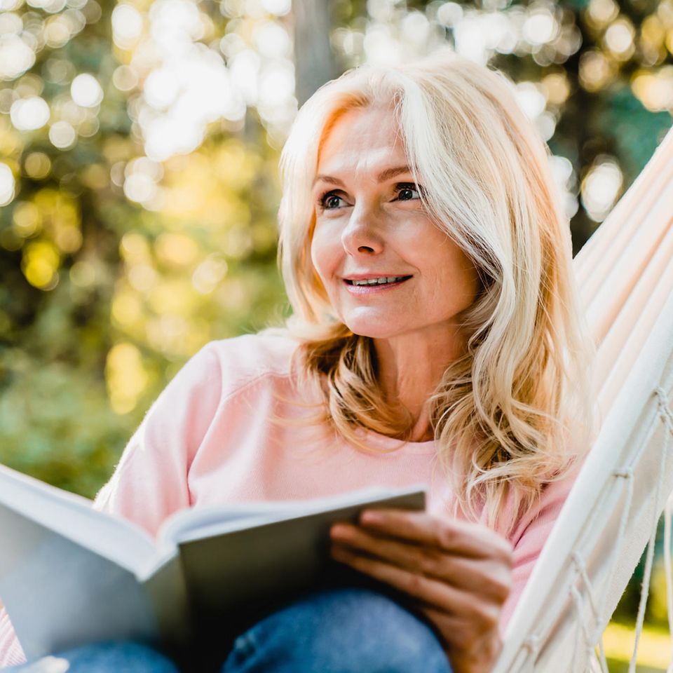 Frau mittleren Alters sitzt im Garten und liest