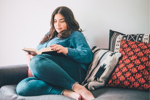 Frau liest auf der Couch ein Buch: Diese 5 Gewohnheiten haben intelligente Frauen