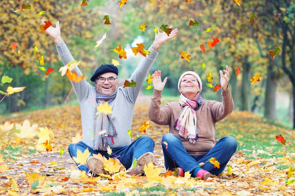 Ein Mann und eine Frau sitzen auf dem Boden und werfen Blätter in die Luft