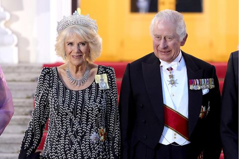 Königin Camilla begeistert an der Seite von König Charles III. beim Staatsbankett im Schloss Bellevue in Berlin mit modischem Stilgefühl, das aber auch die Tradition wahrt. Ihre bodenlange Robe von Bruce Oldfield ist mit ihrer eleganten Silhouette und den rankenförmigen Stickereien in Weiß bereits ein Blickfang. Aber auch der gewählte Schmuck ist bemerkenswert. Camilla trägt die beeindruckende Greville Tiara, auch bekannt als Boucheron Honeycomb Tiara, die sie einst von der verstorbenen Queen Elizabeth II. geschenkt bekam. Dazu setzt sie auf eine strahlende Diamantkette, welche ihre verstorbene Schwiegermutter 1947 zur Hochzeit erhielt. Auf ihrer linken Schulter erreicht die Würdigung an die Queen den Höhepunkt: Ein Familienorden mit Porträt unterstreicht Camillas Verbundenheit deutlich.