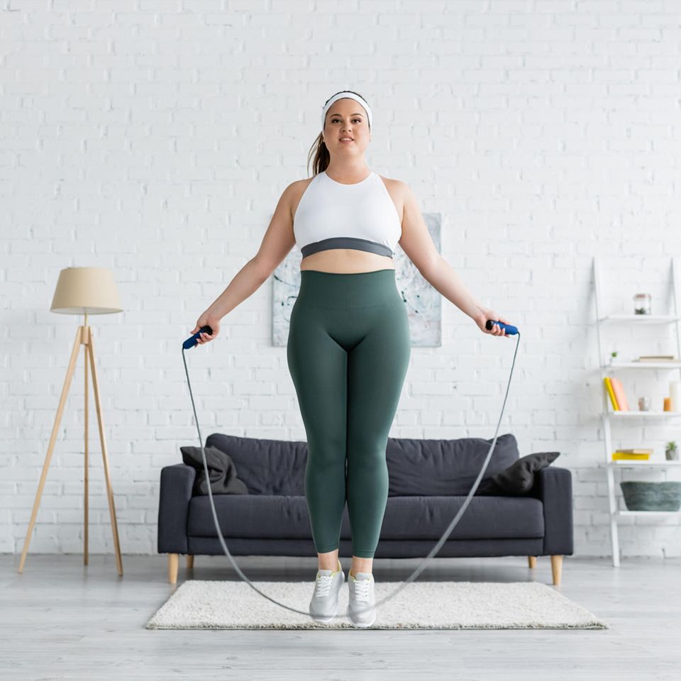 Frau springt Seil im Wohnzimmer: So oft pro Woche solltest du wirklich Sport machen