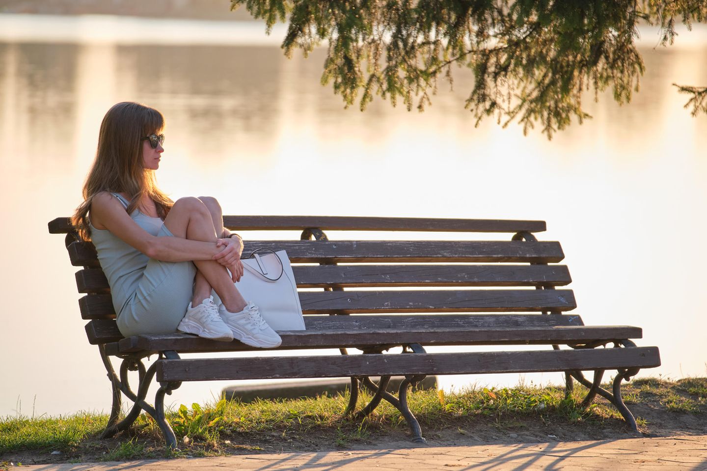 Psychologie: Eine nachdenkliche Frau auf einer Bank am See