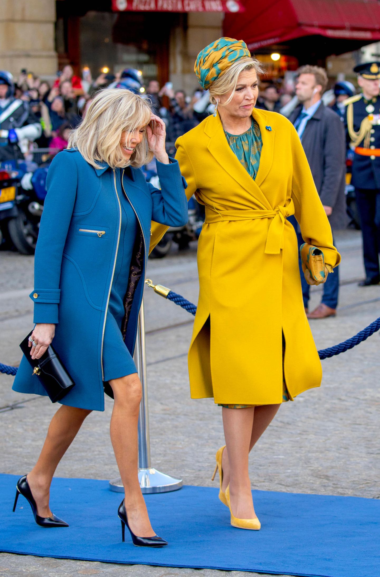 Willkommen in Amsterdam! Das niederländische Königspaar empfängt den französischen Premierminister Emmanuel Macron und seine Frau Brigitte für einen zweitägigen Besuch in der Hauptstadt. Und wie es aussieht, harmonieren Máxima und die Première Dame mit ihren Outfits schon vom ersten Moment an. Das mattblaue Ensemble mit Etuikleid und Mantel passt hervorragend zum senfgelben Mantel von Natan Couture, unter dem die Königin ein grüngoldenes Kleid mit passender Kopfbedeckung trägt.
