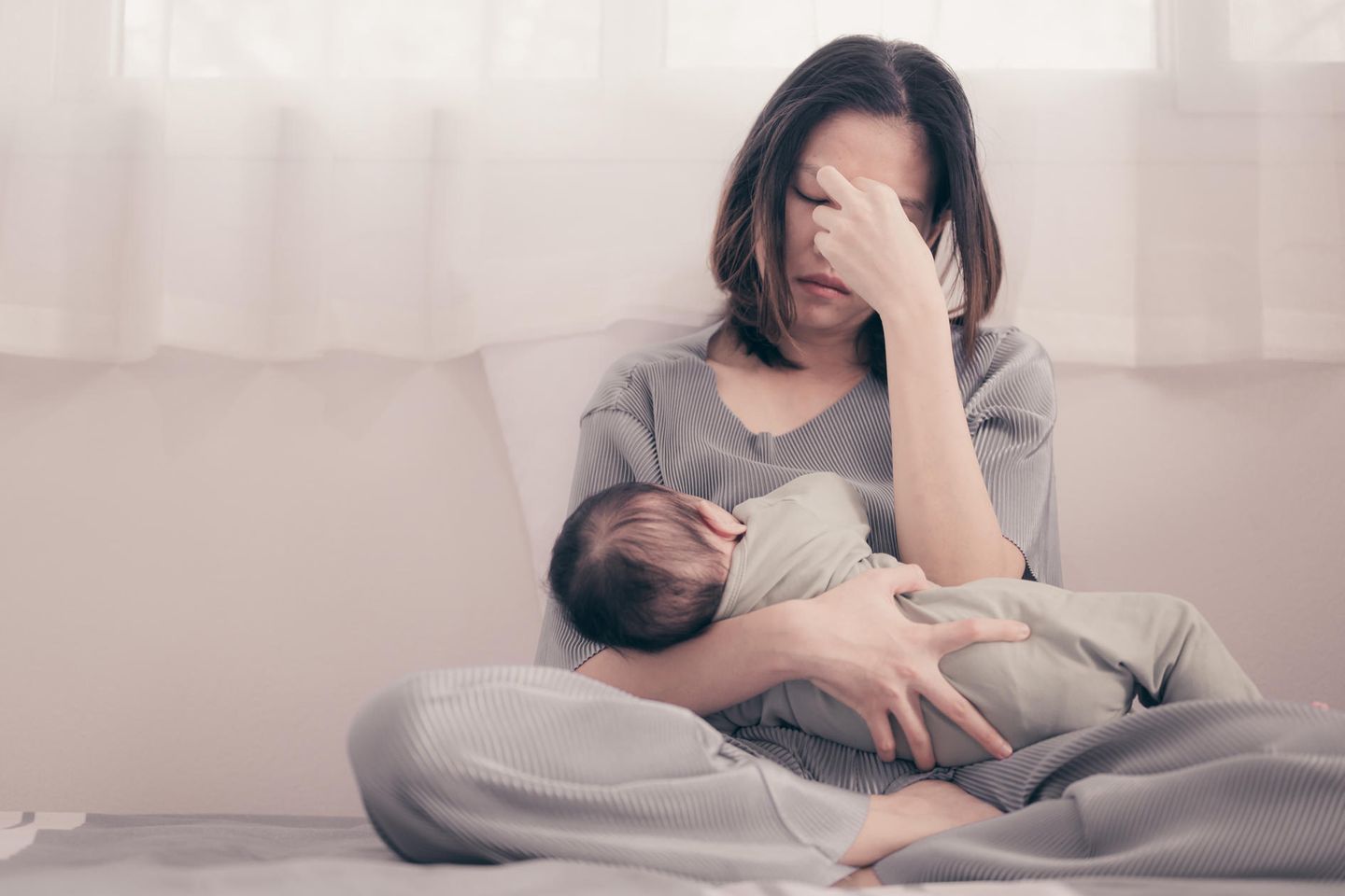 Faces of Moms: Eine erschöpfte junge Frau mit einem Säugling im Arm