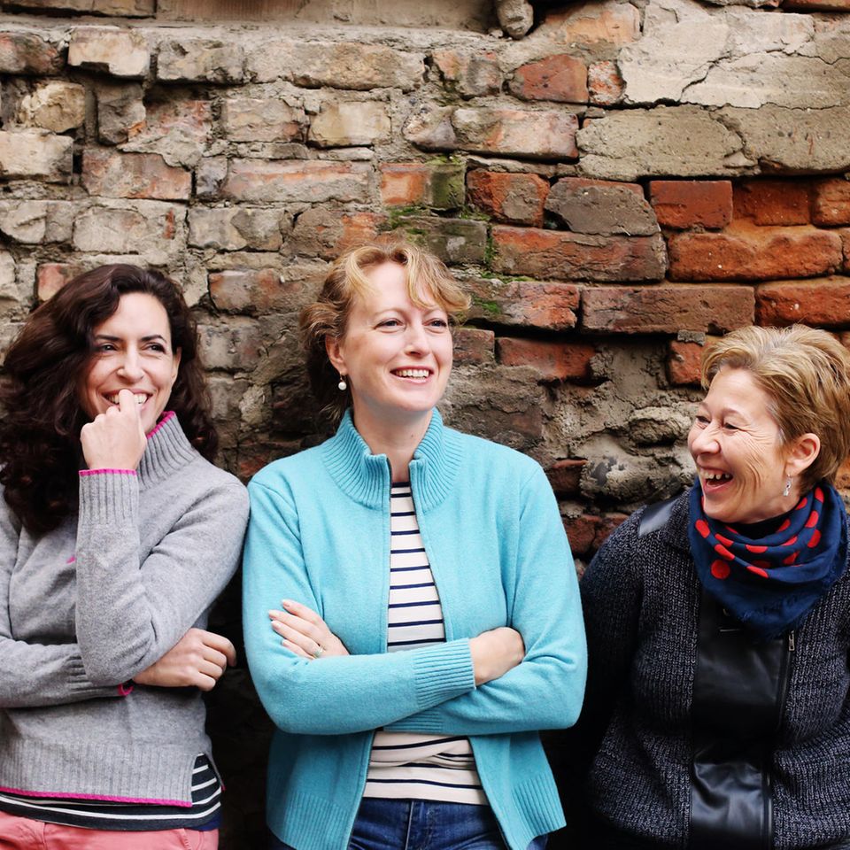 Drei Freundinnen stehen angelehnt an einer Wand und lachen.