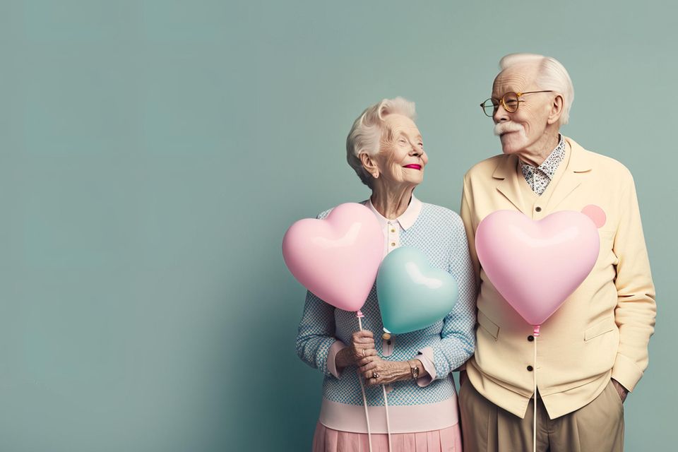 Ein älteres Ehepaar hält Herzluftballons in der Hand.