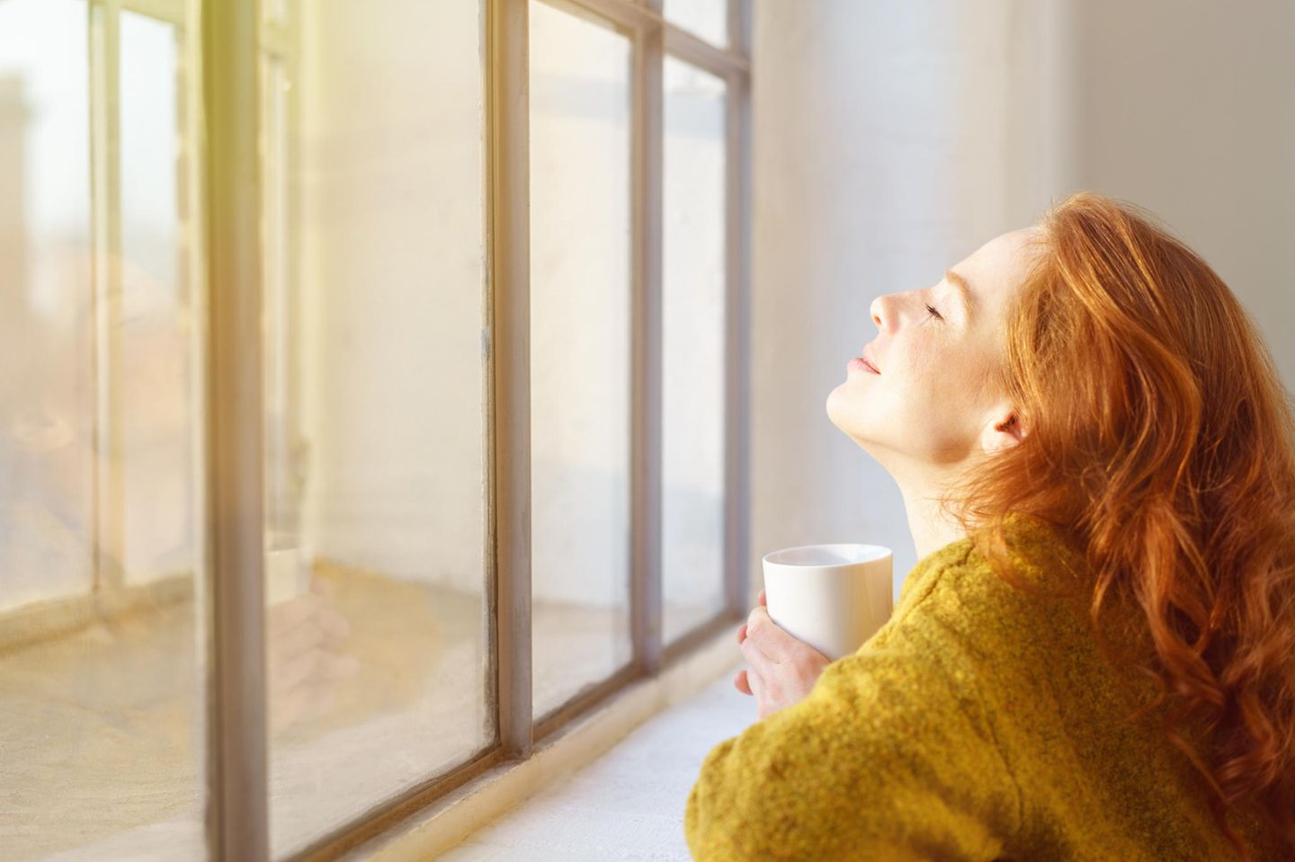 Eine Frau sitzt entspannt an ihrem Fenster und genießt die Sonne