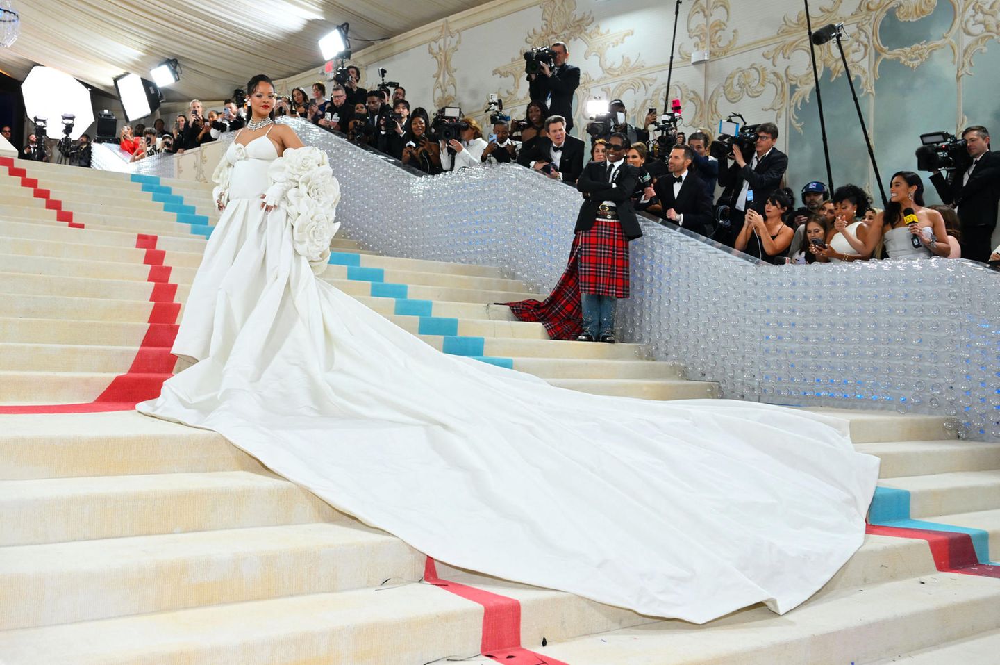 In weißer Robe und opulenter Jacke mit Kamelienblüten von Valentino begeistert Rihanna auf dem Red Carpet. Die zahlreichen Blumen bilden dabei eine wunderschöne Hommage an Chanel und drapieren sich adrett um ihren Babybauch. 
