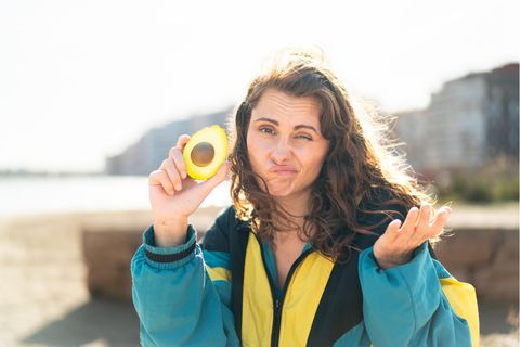 Klimakolumne: Eine Frau schaut fragend in die Kamera und hält eine halbe Avocado