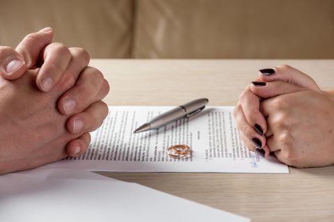 Frauenkolumne: Zwei paar Hände liegen gefaltet links und rechts von einem Dokument, auf dem Eheringe liegen