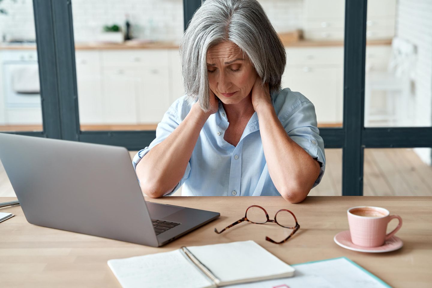 Frau sitzt vor einem Laptop und hält sich am Nacken