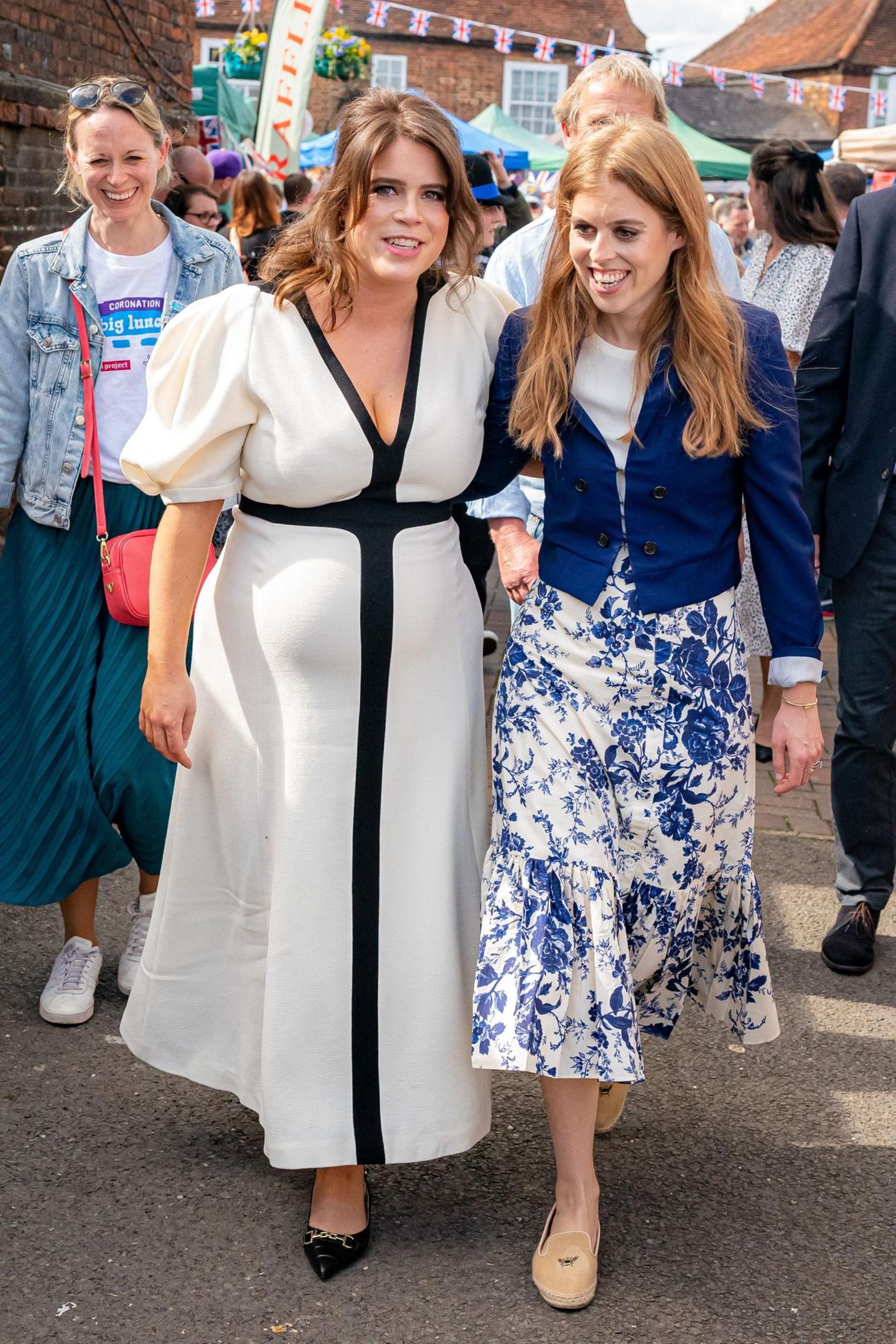 Die Krönungsfeierlichkeiten gehen weiter! Prinzessin Beatrice und Prinzessin Eugenie zeigen sich freudestrahlend in der Grafschaft Buckinghamshire zum großen "Coronation Lunch" mit dem Volk. Für den süßen Schwesternauftitt wählt Beatrice einen blau-weißen Blumenrock von Cara Cara und kombiniert ihn mit einem blauen Blazer von McQ by Alexander McQueen. Ihre jüngere Schwester, die aktuell mit dem zweiten Kind schwanger ist, setzt auf ein schwarz-weißes Midikleid von Gabriela Hearst.