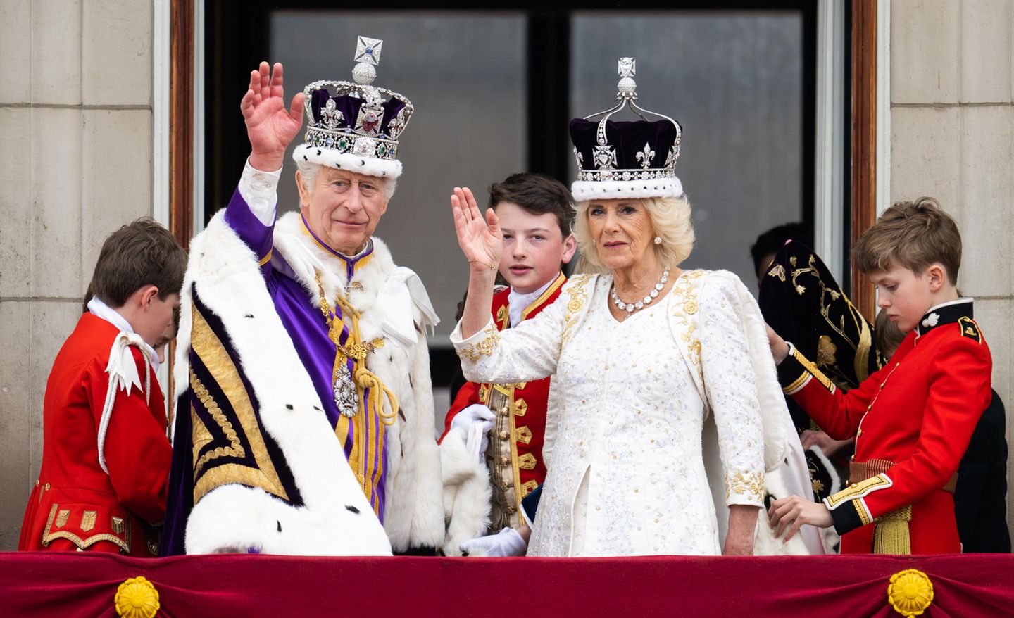 God save the King! Auf dem Balkon des Buckinghampalastes winken der neu gekrönte König und seine Königsgemahlin dem Volk zu. Für dieses Ereignis hat sich Charles noch einmal umgezogen, trägt zum weißen Hemd mit Distelstickereien eine Jacke in Purpur – noch heute noch der teuerste Farbstoff und ein Symbol des Adels. Königin Camilla bleibt in ihrem Krönungsoutfit und strahlt im A-Linien-Kleid mit 3/4-Ärmeln und goldenen Details von Bruce Oldfield.