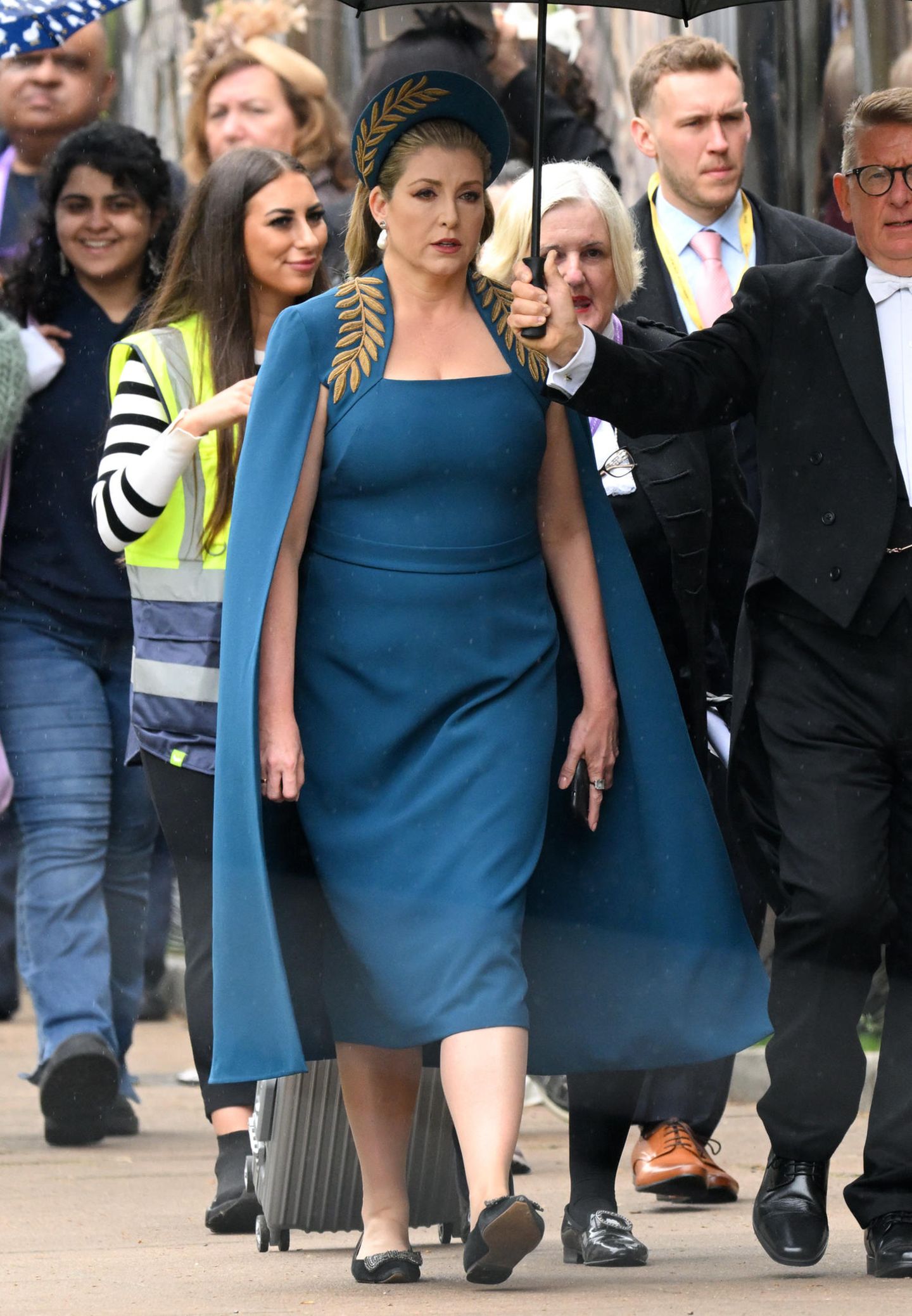 Sie legt einen echten Überraschungsauftritt hin: Penny Mordaunt, Präsidentin des britischen Unterhauses, darf als erste Frau in der britischen Geschichte das Sword of State, also das Staatsschwert, als Teil der Insignien in die Kirche tragen. Doch nicht nur damit dürfte sie den meisten Zuschauer:innen der Krönung im Gedächtnis bleiben. In einem petrolfarbenen Kleid mit gleichfarbigem Cape und den imposanten Haarreif, der ihr blondes Haar während der wichtigen Aufgabe zurückhält, zieht sie zusätzlich die Blicke auf sich. 