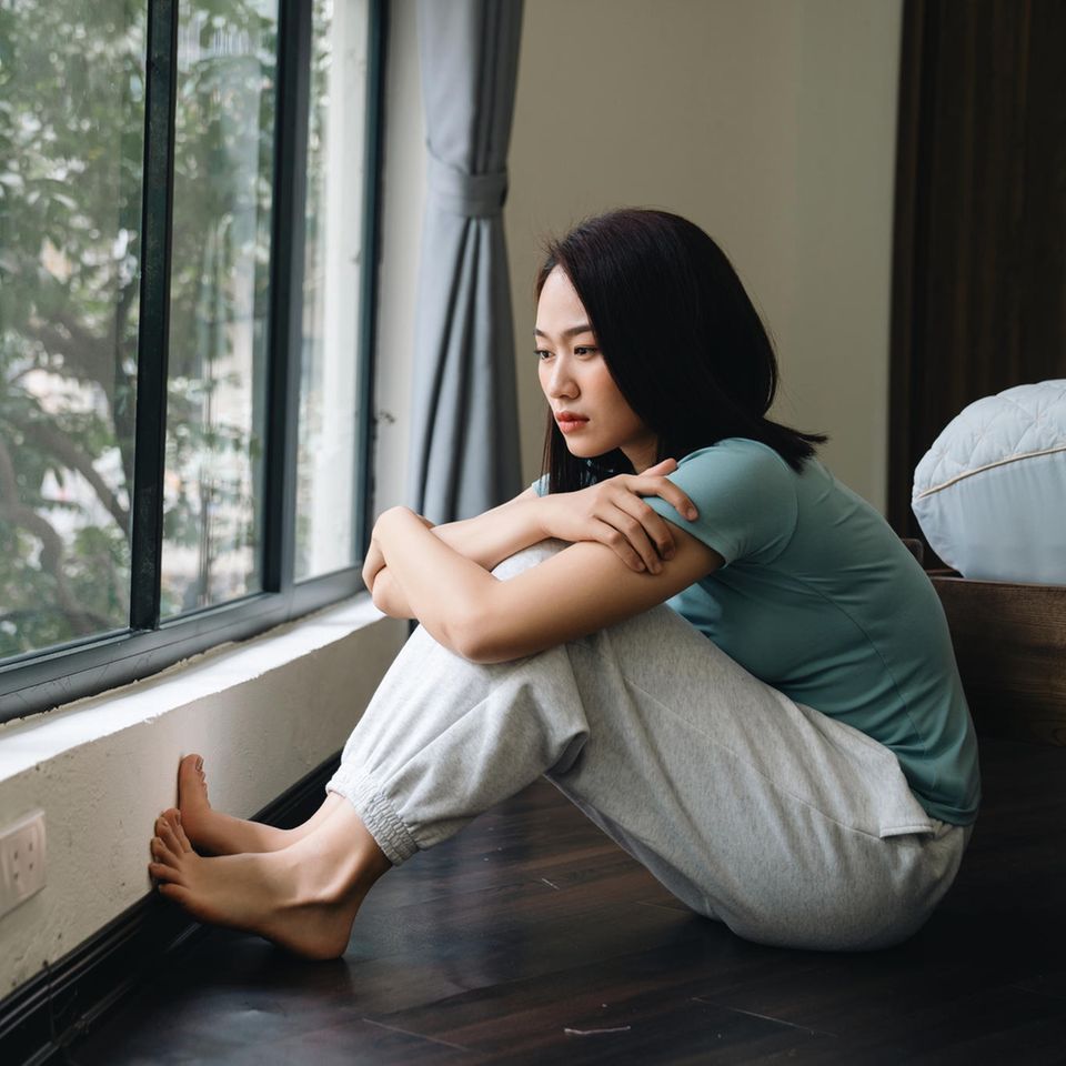 Danxiety: Junge Frau sitzt auf Fußboden vor Fenster und schaut hinaus