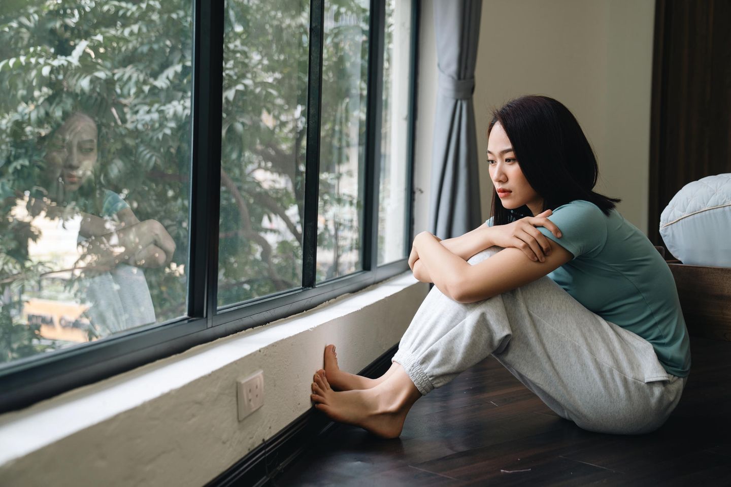 Danxiety: Junge Frau sitzt auf Fußboden vor Fenster und schaut hinaus