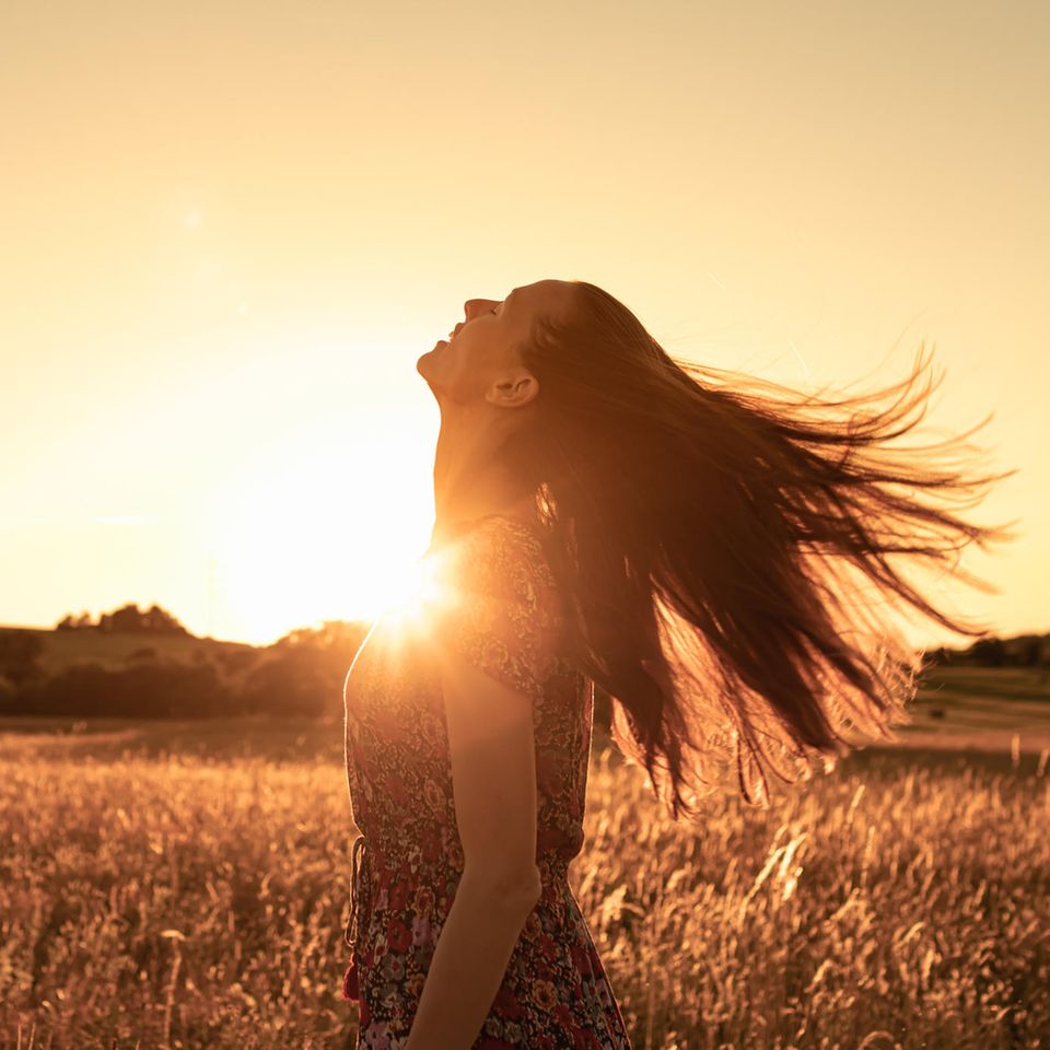 Eine Frau im Sommerkleid steht im Licht der untergehenden Sonne