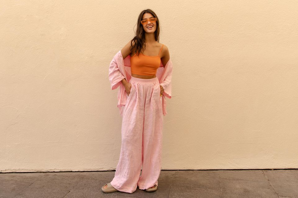 Die perfekte Sommerhose: Junge Frau in sommerlichem Outfit steht vor einer hellen Wand