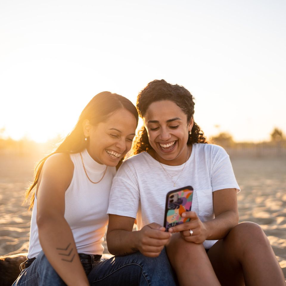 Zwei Frauen sprechen und schauen auf ein Handy: 4 Tipps, mit denen du es deinem Gegenüber leichter machst, sich zu öffnen