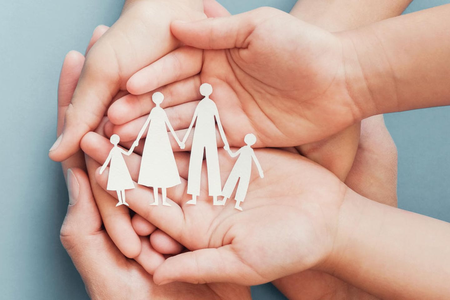 Pflegekind: Hände halten die ausgeschnittenen Silhouetten einer Familie aus Papier
