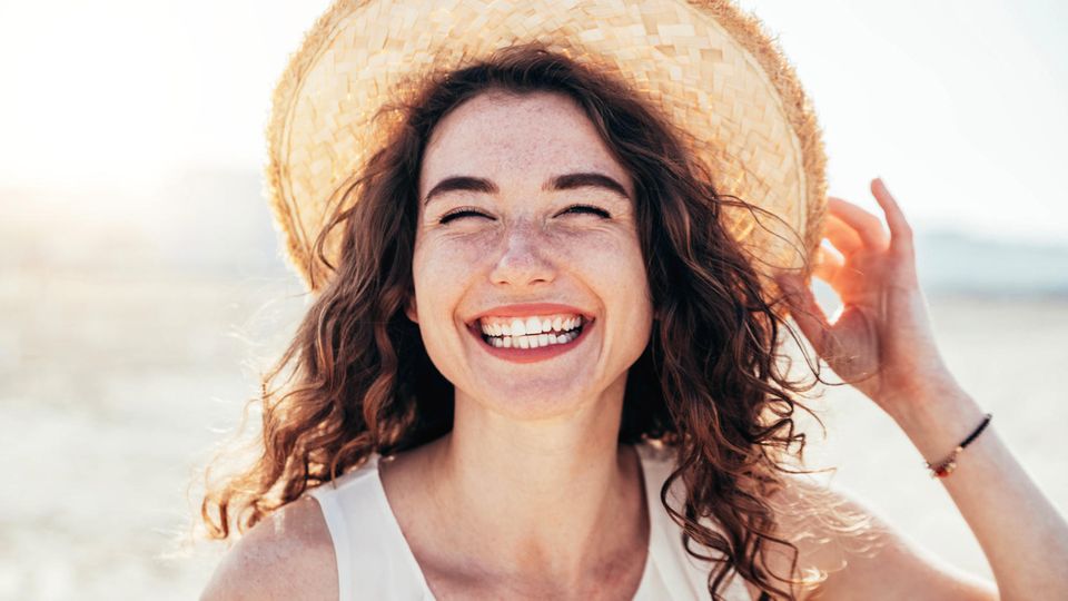 Horoskop ab 22.5.: eine fröhliche Frau mit Hut
