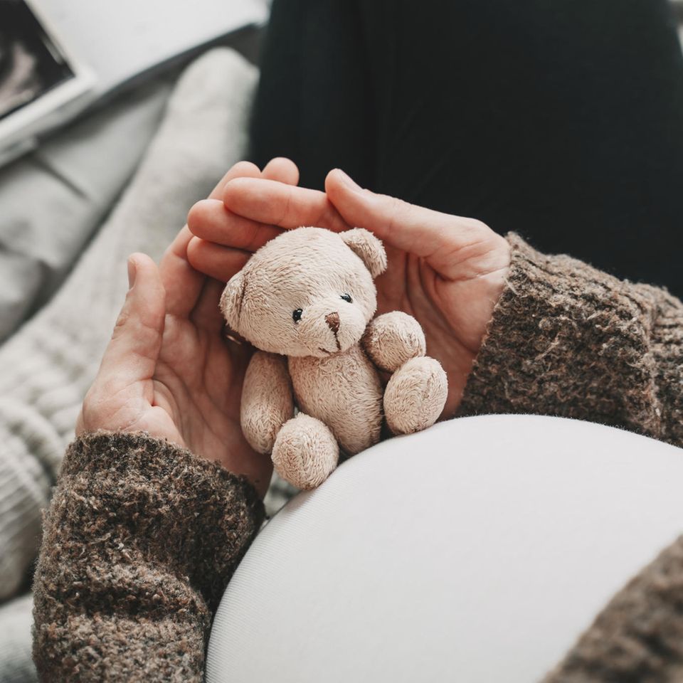 Frau mit Babybauch hält Teddy.