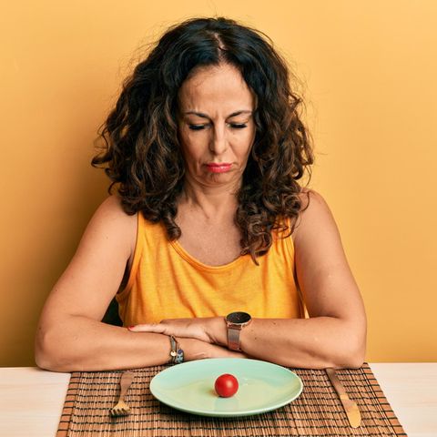 Gewichtszunahme in den Wechseljahren: Frau schaut enttäuscht auf die nur eine Tomate auf ihrem Teller