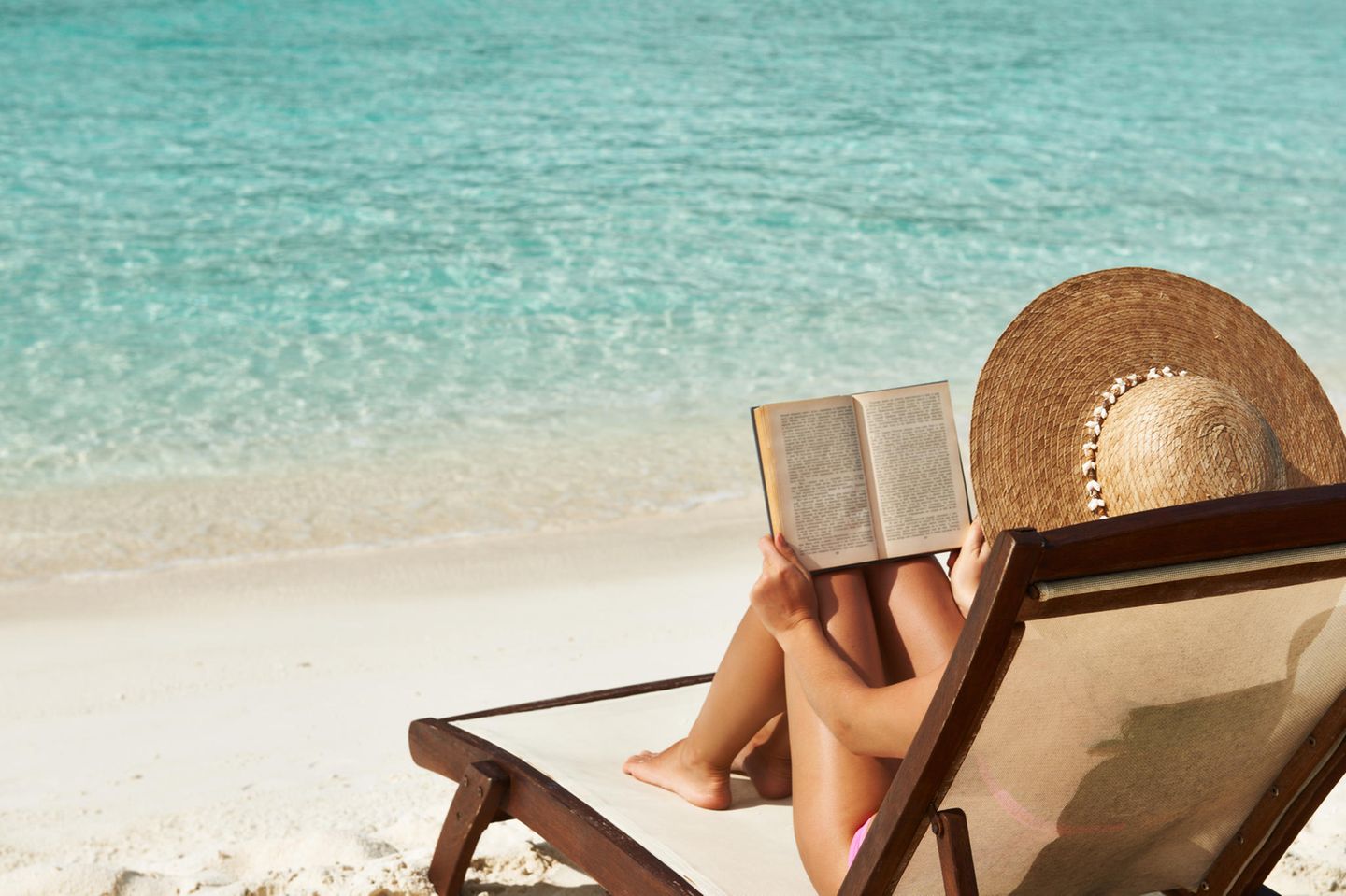 Frau liest ein Buch am Strand in der Sonne, Buchtipps Sommer