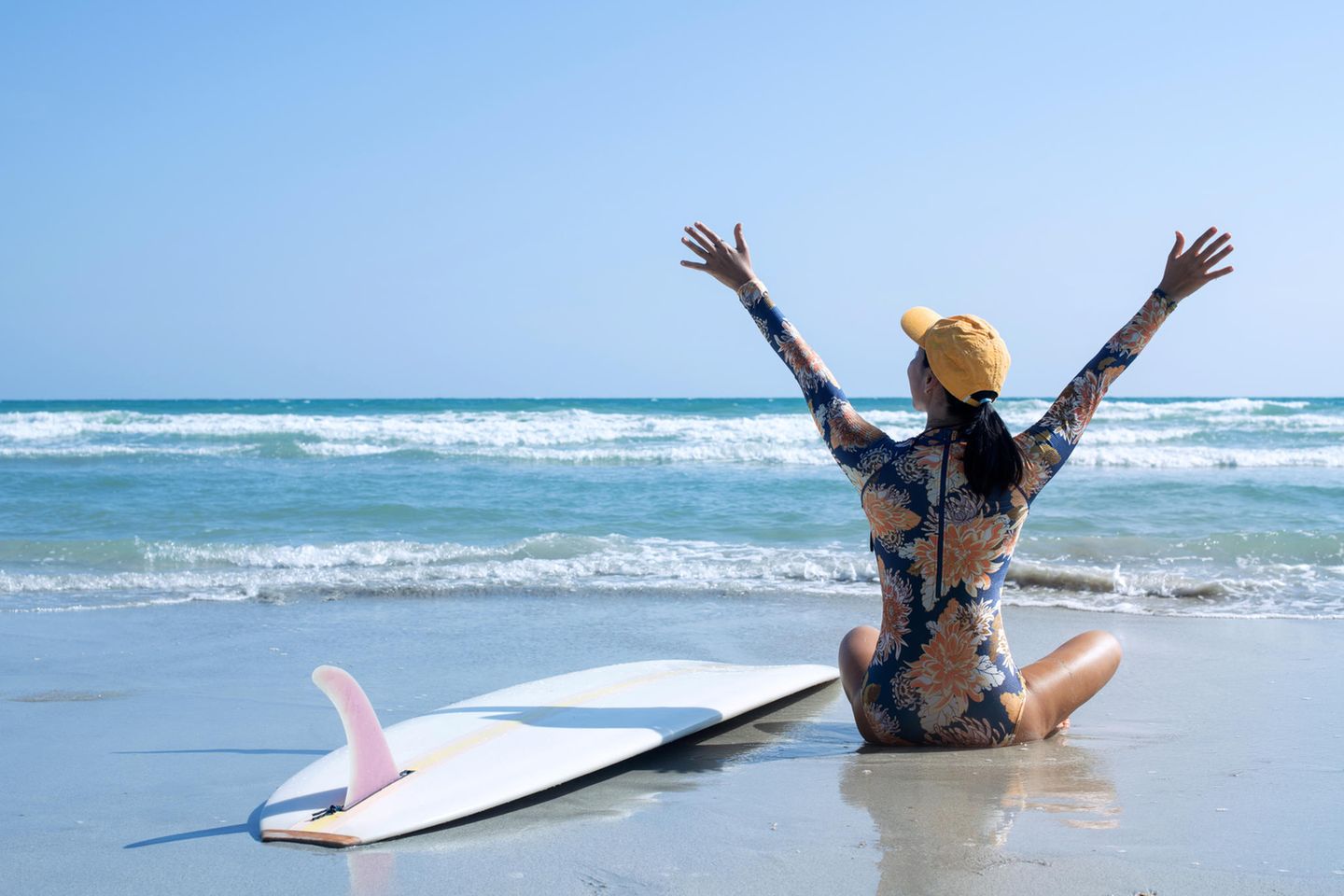 Surf-Badeanzug: Die perfekte Beachwear für einen aktiven Tag auf dem Wasser, Frau am Strand mit Surfbrett und Meer