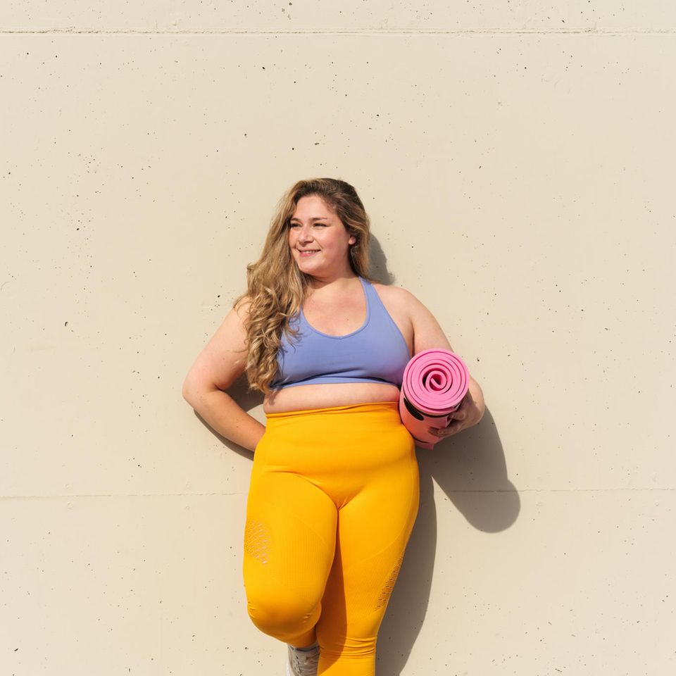 Sportliche Frau steht an einer Mauer: Sind 5 Minuten Sport pro Tag genug, um fit zu bleiben?