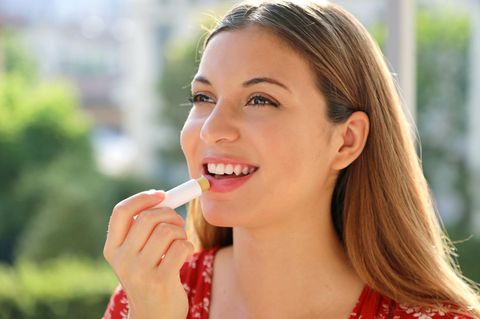 Sonnenschutz für die Lippen: Glückliche junge Frau benutzt Lippenpflegestift