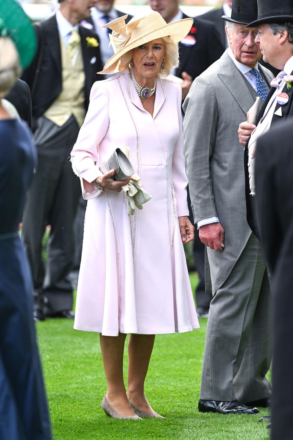 Was für eine puderrosa Überraschung! Für die Tagesveranstaltung in Ascot setzt Königin Camilla auf ein blassrosa Mantelkleid von Anna Valentine – und das trug sie schon bei einem ganz besonderen Event zuvor. Der Hochzeit von Prinz Harry und Meghan. Ihren schönen Recycler-Look garniert die Frau von König Charles mit einem vanillefarbenen Hut von Philip Treacy.