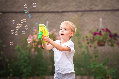 Seifenblasenpistole: 8 coole Modelle für Kinder, Junge mit Seifenblasen im Garten