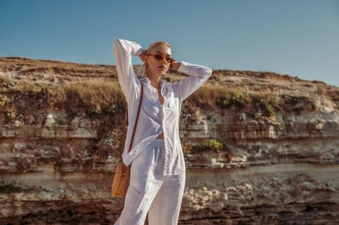 Das perfekte Sommeroutfit: Eine Frau im weißen Leinenoutfit auf einer Klippe