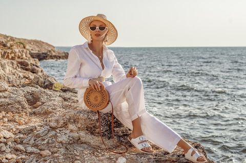 Die perfekten Sandalen: Eine Frau sitzt in sommerlichem Outfit auf einer Klippe