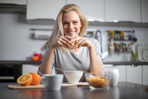 Frühes Frühstück ist gesünder: Blonde junge Frau sitzt am Frühstückstisch mit einem Glas Orangensaft in der Hand