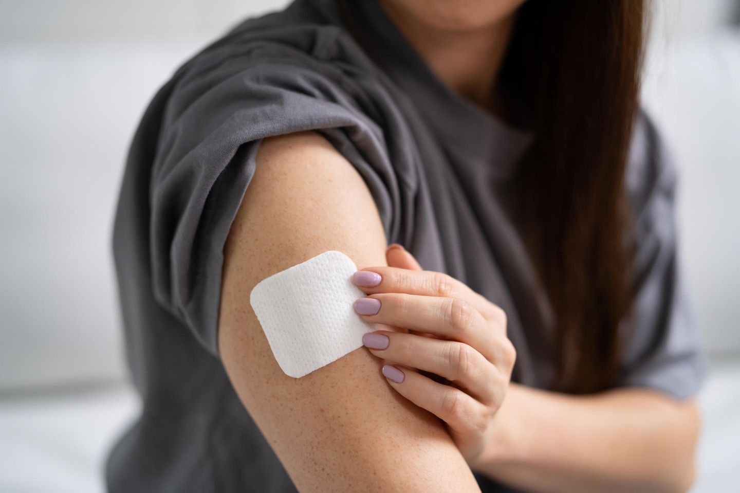 Hormonersatzherapie: Eine Frau im grauen T-Shirt befestigt ein Hormonpflaster auf ihrem Oberarm