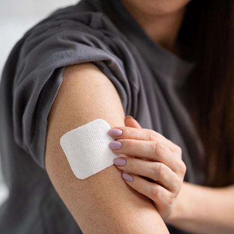 Hormonersatzherapie: Eine Frau im grauen T-Shirt befestigt ein Hormonpflaster auf ihrem Oberarm