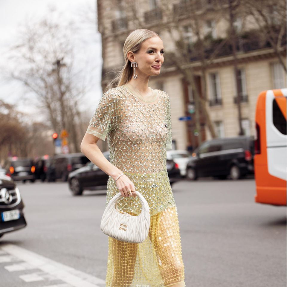 Influencerin Leonie Hanne liebt sie und wir auch: Die Miu Miu Wander Bag ist die Trendtasche schlechthin! Auf der Pariser Fashion Week kombiniert die gebürtige Hamburgerin zu ihrem transparenten Glitzerkleid das 1.950 Euro teure It-Piece in Weiß.