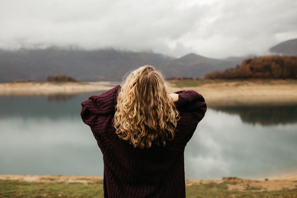 Gestresste Frau vor einem See: Diese 4 selbstzerstörerischen Verhaltensweisen können auf Angst zurückzuführen sein