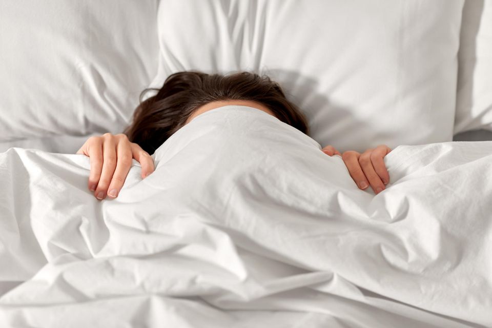 Frau liegt im Bett mit Decke überm Kopf