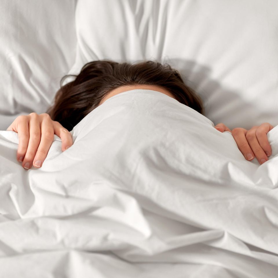 Frau liegt im Bett mit Decke überm Kopf
