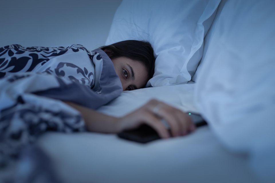 Eine Frau liegt schlaflos im Bett und hält ihr Handy